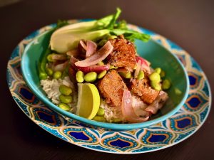 Turquoise bowl with pan-friend tofu on top of white basmati rice, with green edamame beans, red onion petals and a lime wedge.