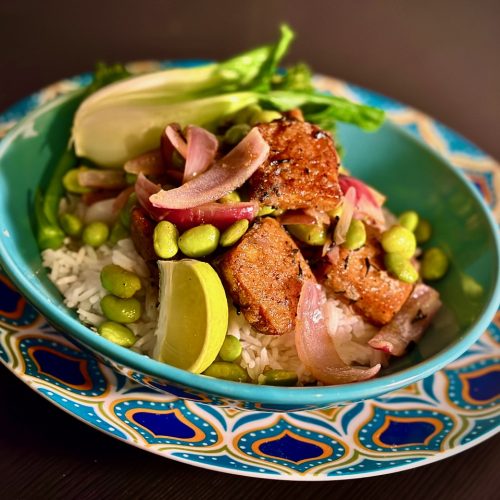 Turquoise bowl with pan-friend tofu on top of white basmati rice, with green edamame beans, red onion petals and a lime wedge.
