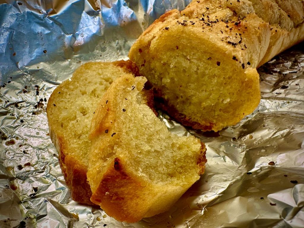 Garlic baguette on top of tin foil with a couple of pieces lying on the side; one piece has a bite out of it
