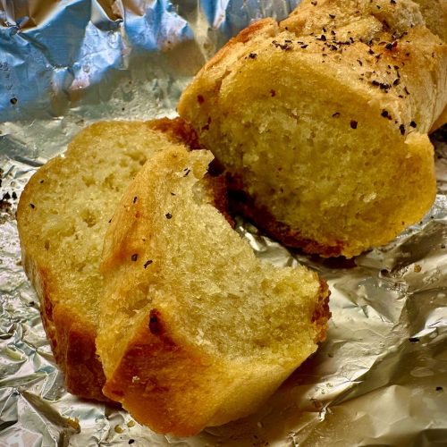 Garlic baguette on top of tin foil with a couple of pieces lying on the side; one piece has a bite out of it