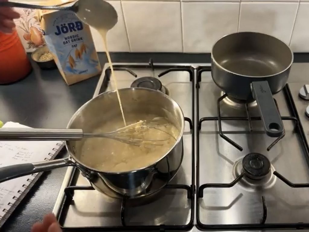 Stainless steel pan on the front left side of a stainsteel hob; the pan has creamy béchamel sauce inside