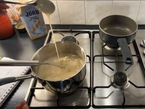 Stainless steel pan on the front left side of a stainsteel hob; the pan has creamy béchamel sauce inside