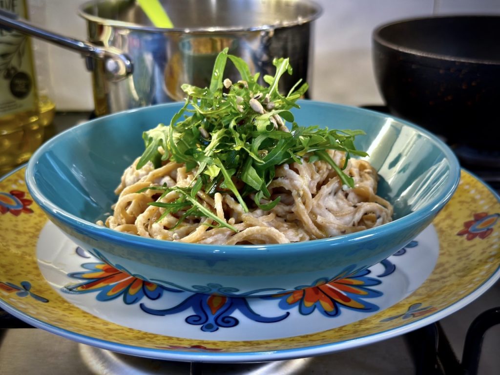 A bowl of wholewheat pasta with creamy alfredo sauce topped with rocket and toasted sunflower seeds
