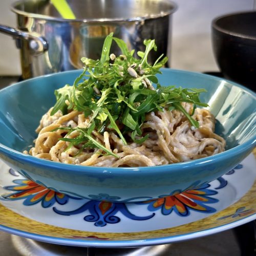 A bowl of wholewheat pasta with creamy alfredo sauce topped with rocket and toasted sunflower seeds