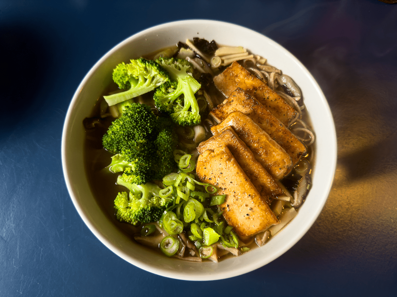 Vegan Ramen: noodles in a clear both, topped with pan-fried tofu, served with broccoli and chopped spring onions