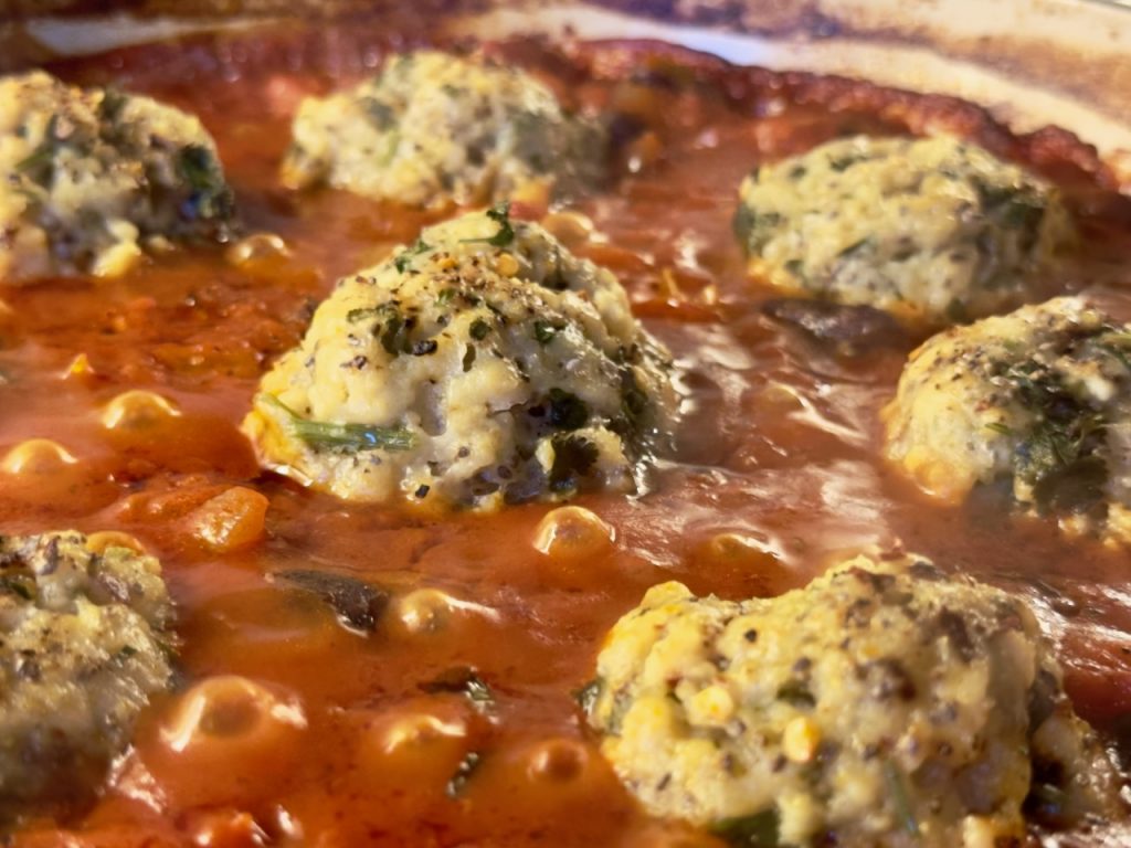 a close up of a rich red tomato and red kidney bean stew with chia seed and herbs dumplings looking light and fluffy and delicious.