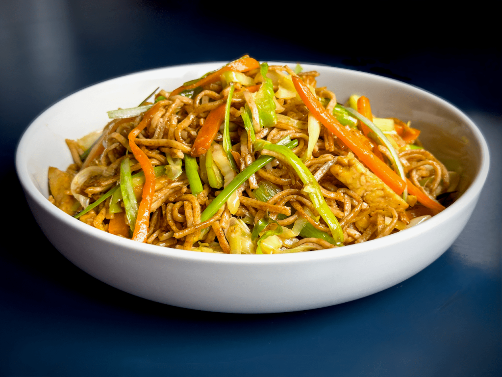 Vegan tempeh chow mein with carrots, spring onions and spring greens