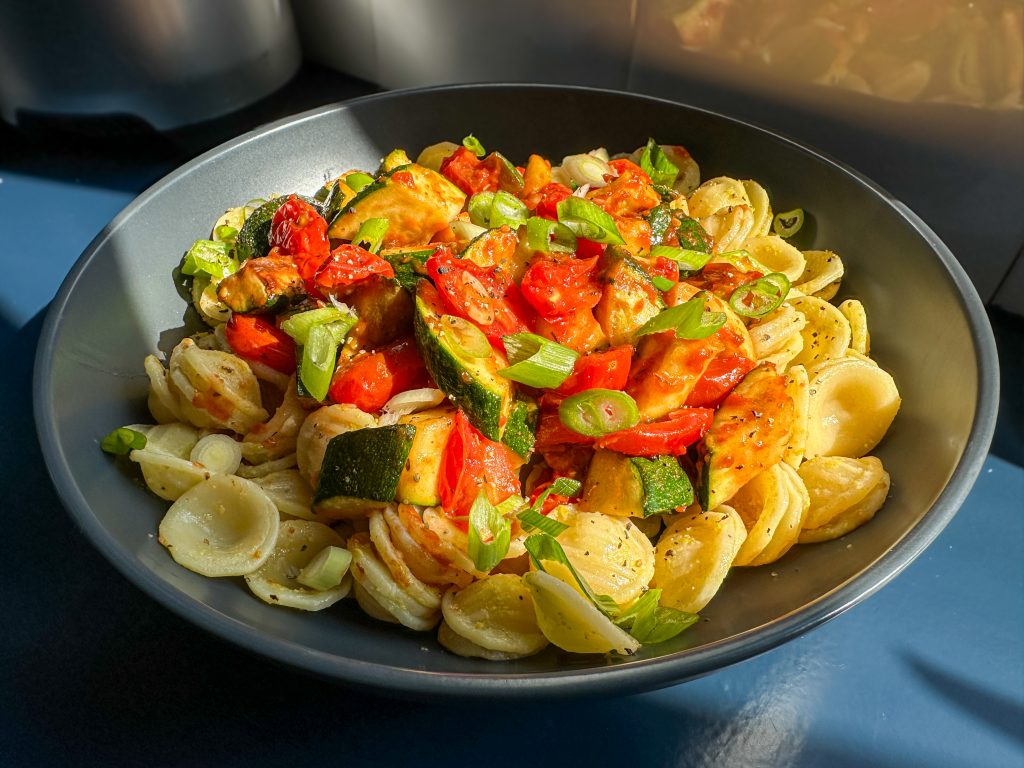 Pasta topped with freshly cooked bright red cherry tomatoes and chunks of courgettes