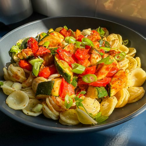Pasta topped with freshly cooked bright red cherry tomatoes and chunks of courgettes