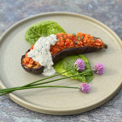 Charred aubergine half topped with red lentils and herbed yoghurt, garnished with fresh herbs on a rustic plate.