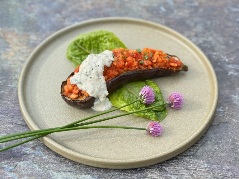 Charred aubergine half topped with red lentils and herbed yoghurt, garnished with fresh herbs on a rustic plate.