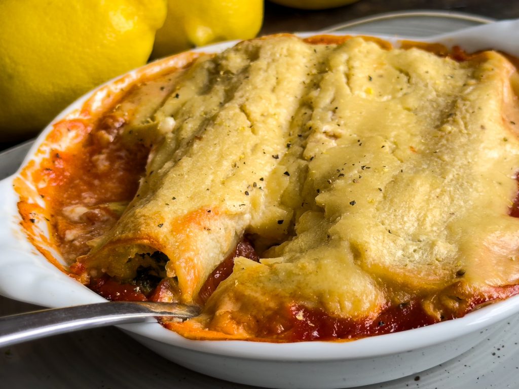 Vegan cannelloni filled with spinach and cannellini, topped with golden lemon-almond cream, served in a white ceramic baking dish.
