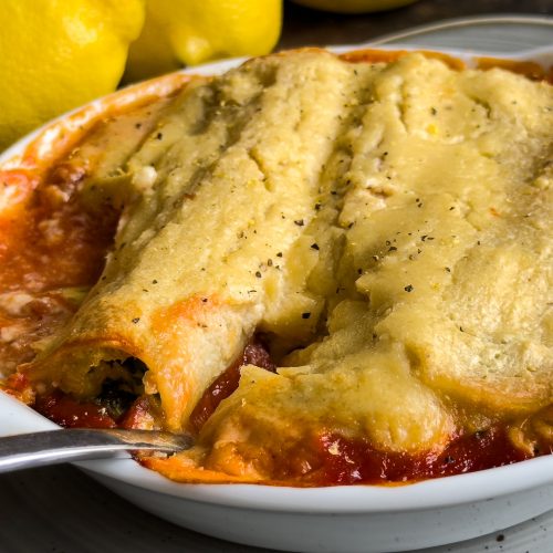 Vegan cannelloni filled with spinach and cannellini, topped with golden lemon-almond cream, served in a white ceramic baking dish.