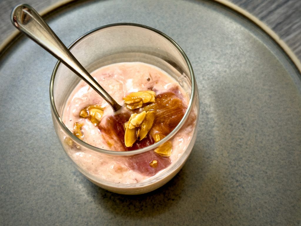a glass of pink rhubarb fool topped with almonds with the spoon in