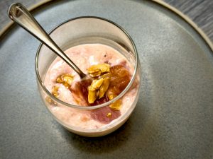 a glass of pink rhubarb fool topped with almonds with the spoon in