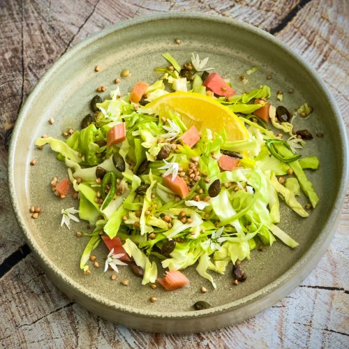 bowl of salad with pumpkin seeds, pickled rhubarb and shaved spring cabbage ribbons, topped with wild garlic flowers