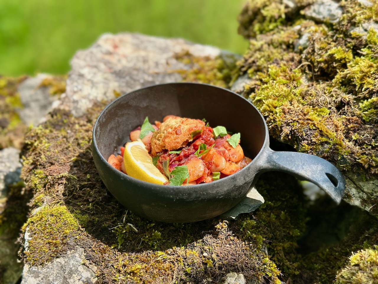 A serviing of sticky barbecue beans and golden cornbread dumplings, with herbs and lemon zest scattered on top