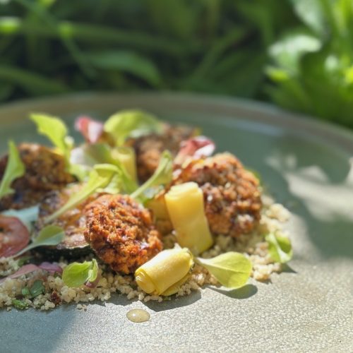 Charred courgette pieces on cous cous with little tofu medallions pan-fried and salad leaves and dots of salad dressing glistening in the sun
