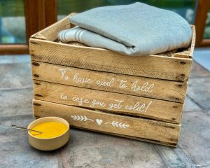 Bowl of red pepper bisque soup in front of lovely decorated wooden crate filled with blankets. A warm cosy image.
