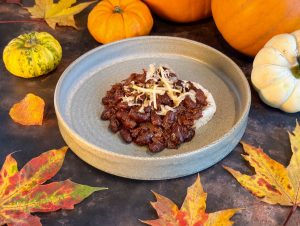 Open stoneware bowl with mash potato topped with rich and dark chill beans, topped with shreds of sauerkraut