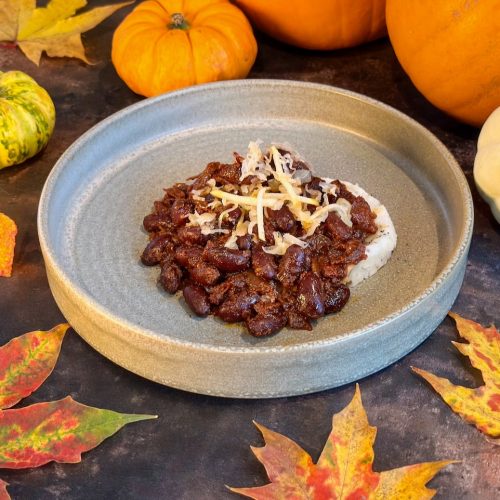 Open stoneware bowl with mash potato topped with rich and dark chill beans, topped with shreds of sauerkraut