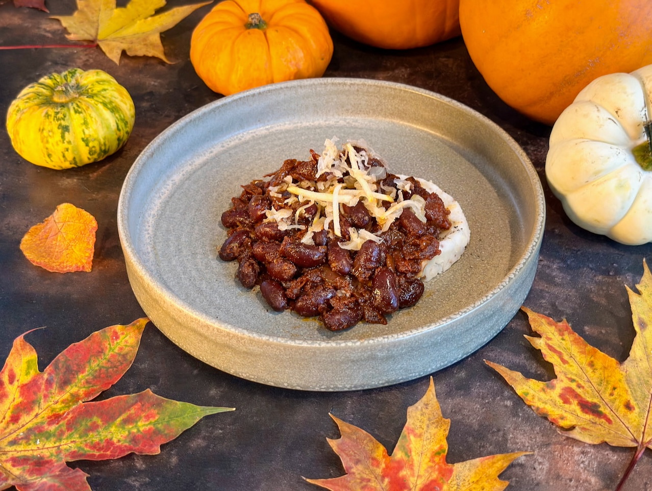 Open stoneware bowl with mash potato topped with rich and dark chill beans, topped with shreds of sauerkraut