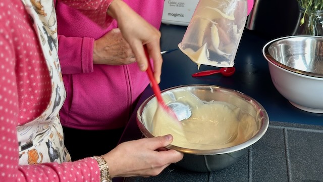 Two women in pink tops making cake batter. You see theirs arms only.