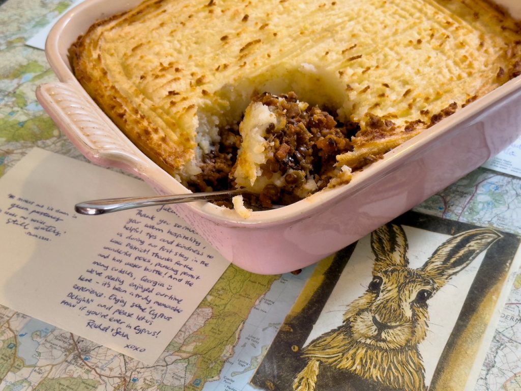a oven dish full of cottage pie with mashed potato. Spoon resting in one corner with a portion of cottage pie resting on the sppn.