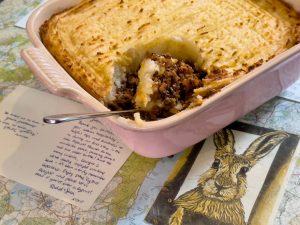 a oven dish full of cottage pie with mashed potato. Spoon resting in one corner with a portion of cottage pie resting on the sppn.