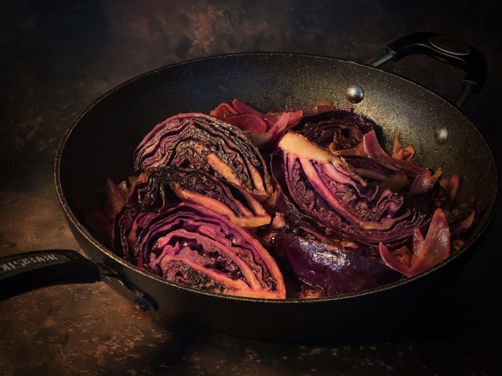 Wedges of red cabbage seared on the edges, in a black pan with orange and apple
