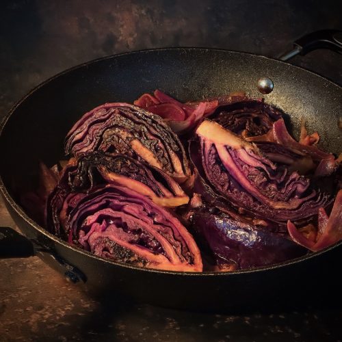 Wedges of red cabbage seared on the edges, in a black pan with orange and apple