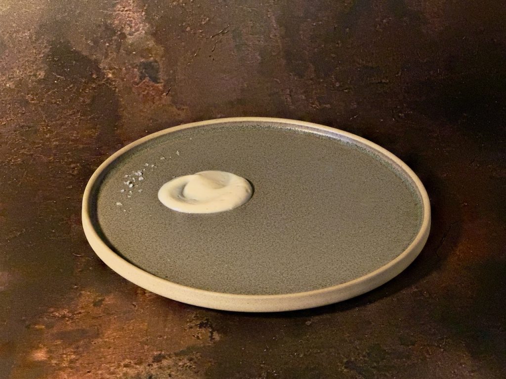 stoneware plate with a neat swirl of smooth shiny tofu cream and a few grains of malden sea salt