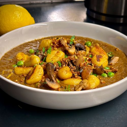 Bowl of mushroom velouté topped with pan-fried gnocchi, mushrooms and peas, with pangrattato and lemon zest