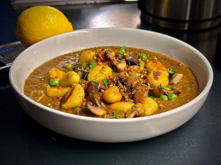 Bowl of mushroom velouté topped with pan-fried gnocchi, mushrooms and peas, with pangrattato and lemon zest